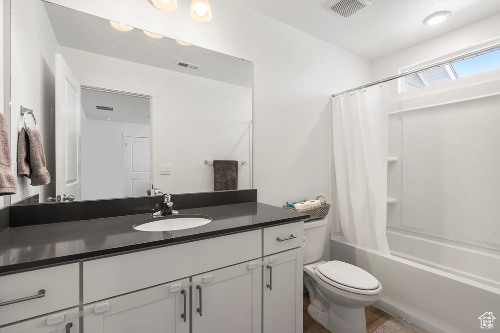 Bathroom with toilet, vanity, shower / bath combination with curtain, and wood finished floors