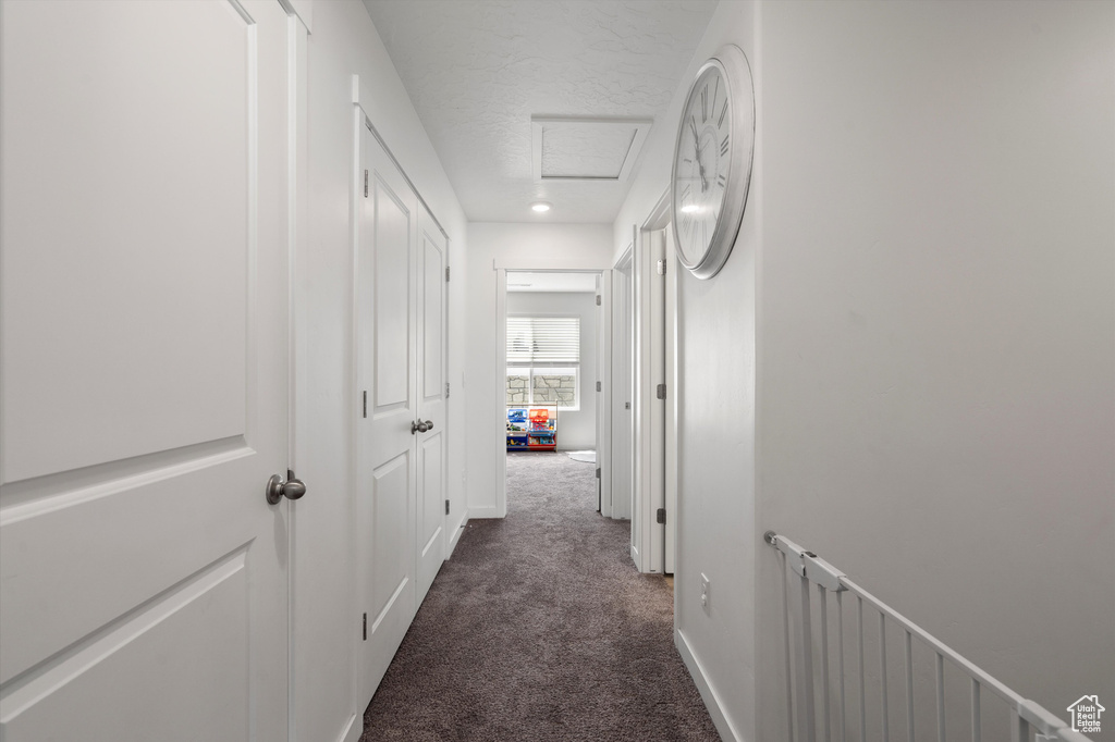 Hallway with dark colored carpet, attic access, baseboards, and a textured ceiling