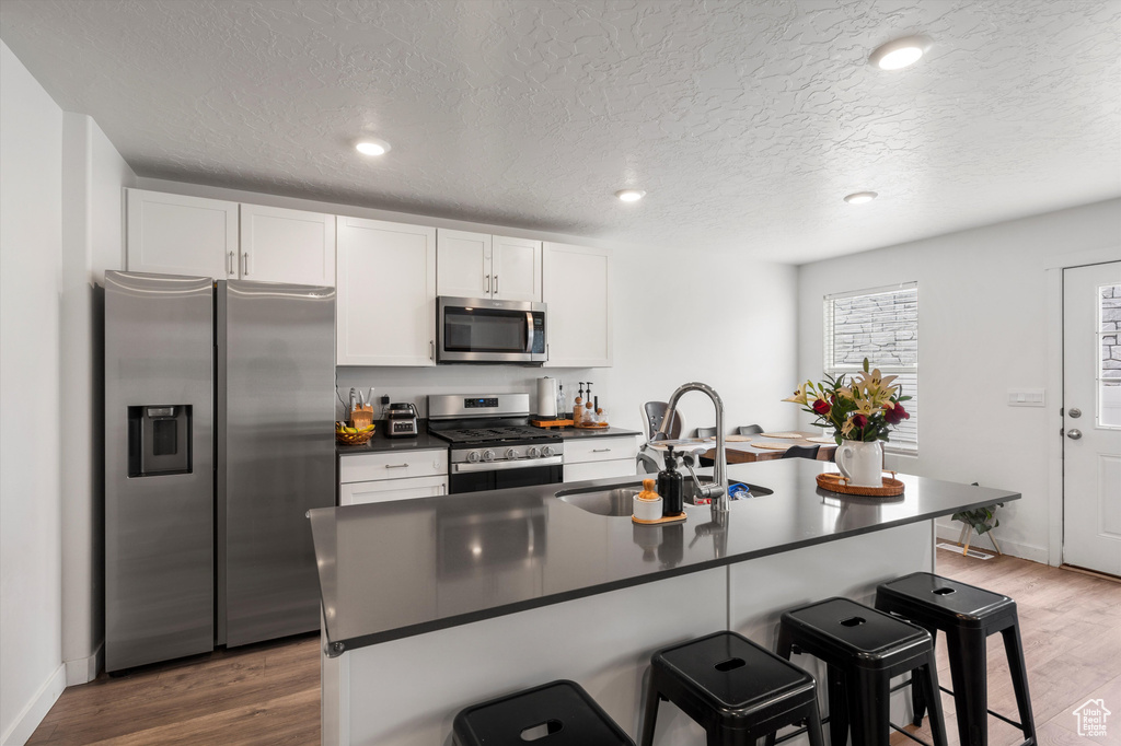 Kitchen with stainless steel appliances, a sink, dark countertops, a breakfast bar, and a textured ceiling