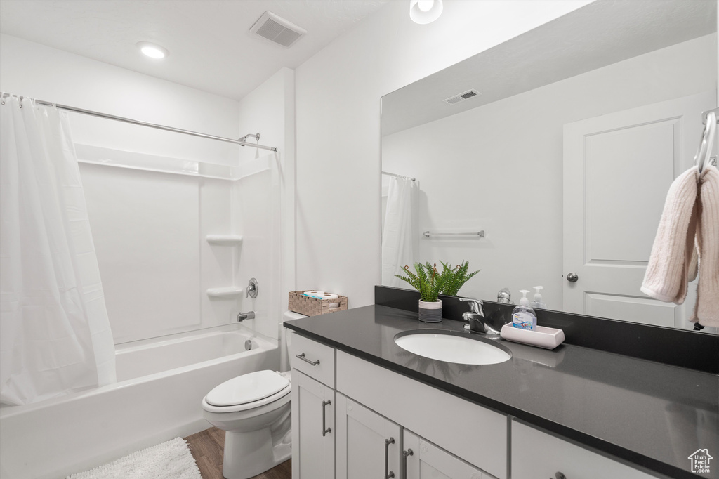 Bathroom with wood finished floors, vanity, shower / bath combo with shower curtain, and toilet