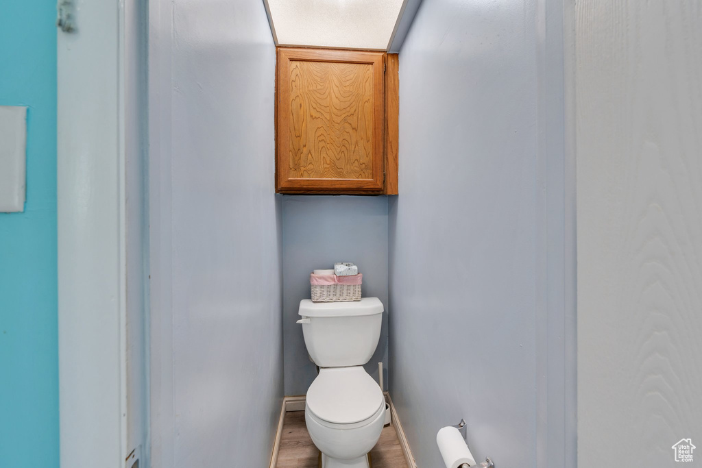 Bathroom featuring wood finished floors, toilet, and baseboards