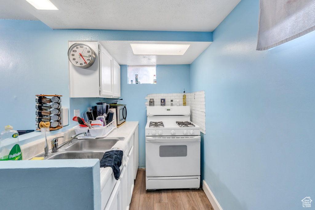Kitchen with white range with gas cooktop, light wood-style flooring, white cabinetry, a sink, and light countertops
