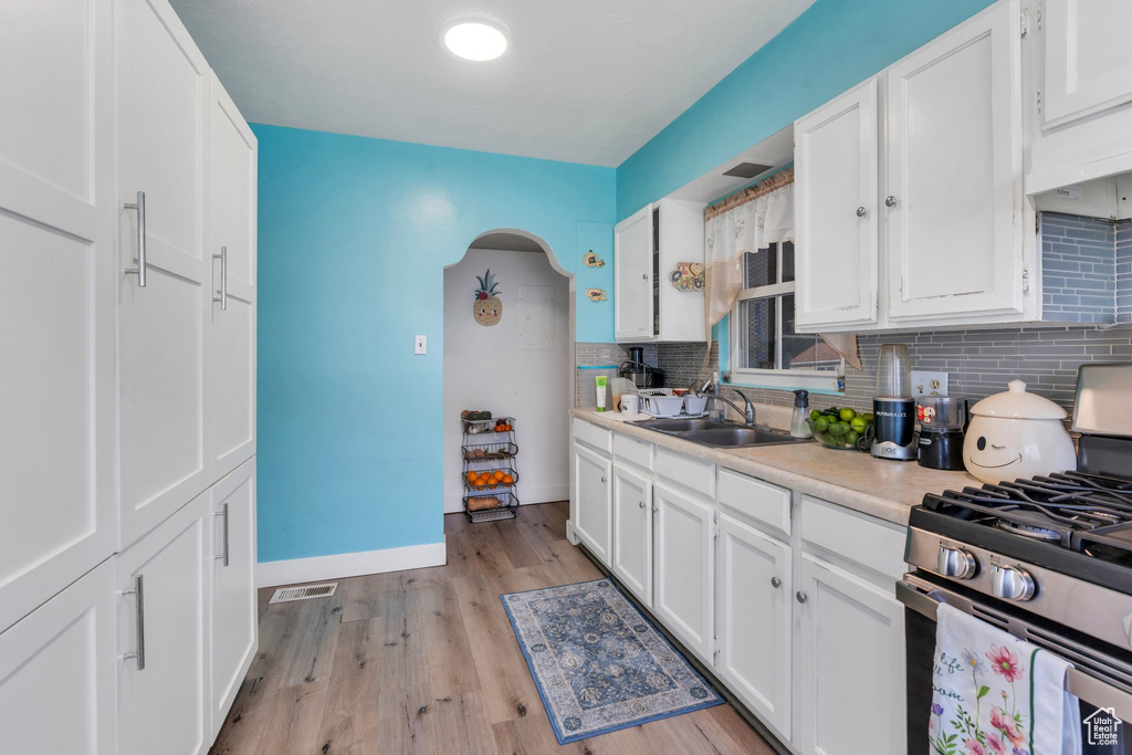 Kitchen with stainless steel range with gas cooktop, a sink, light countertops, decorative backsplash, and white cabinets