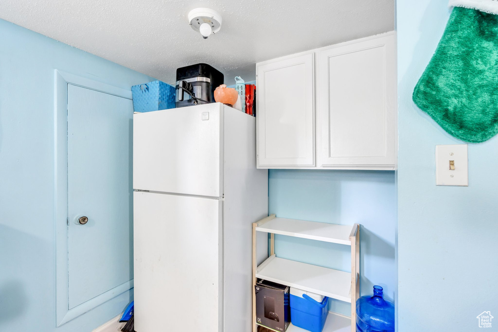 Kitchen featuring freestanding refrigerator, white cabinets, light countertops, and a textured ceiling