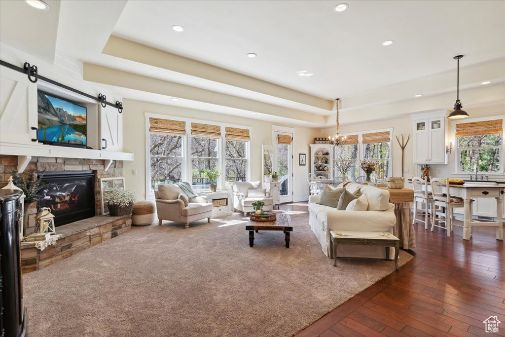 Living room featuring recessed lighting, a tray ceiling, dark wood-style floors, a stone fireplace, and a barn door