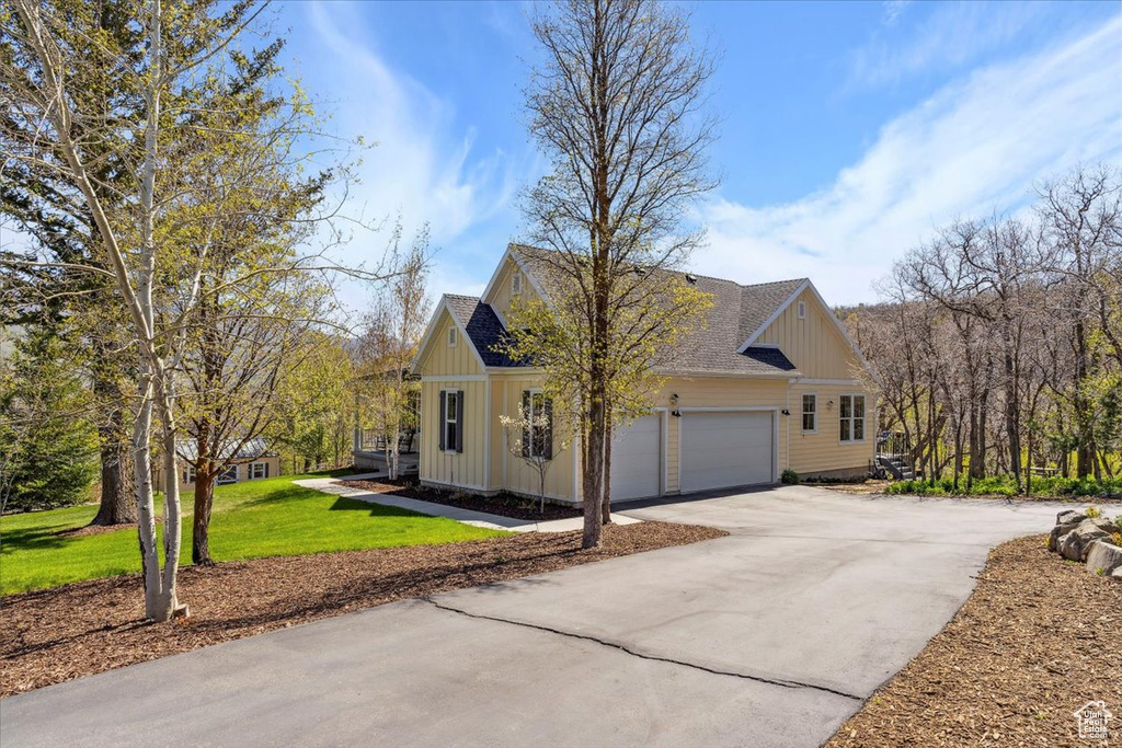 View of property exterior with board and batten siding, driveway, a garage, a yard, and roof with shingles