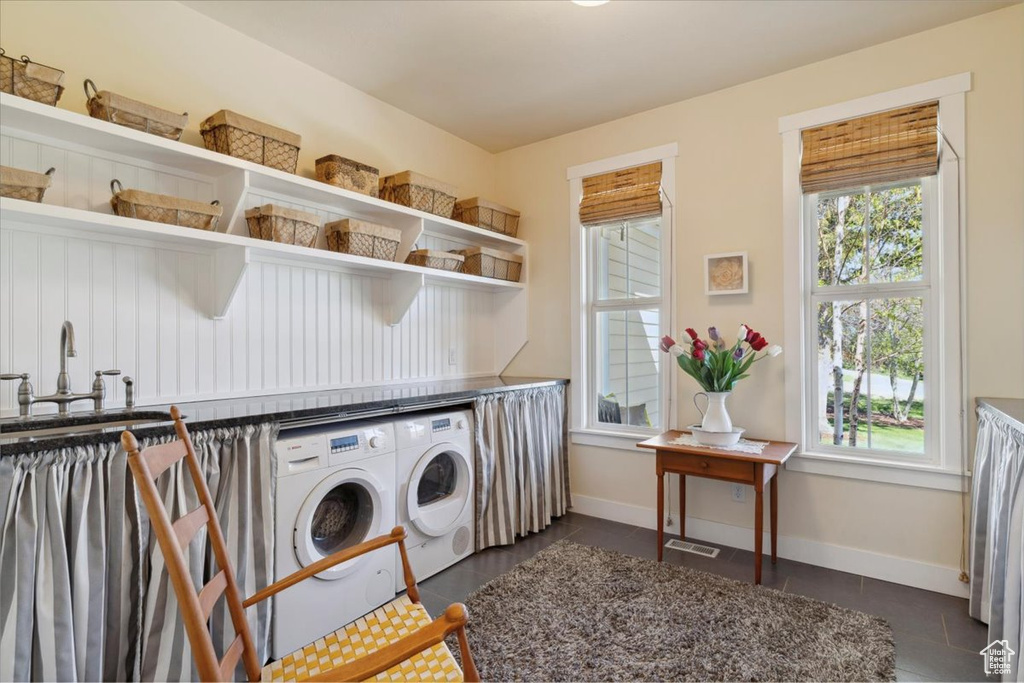 Clothes washing area with washer and clothes dryer, plenty of natural light, baseboards, and dark tile patterned flooring