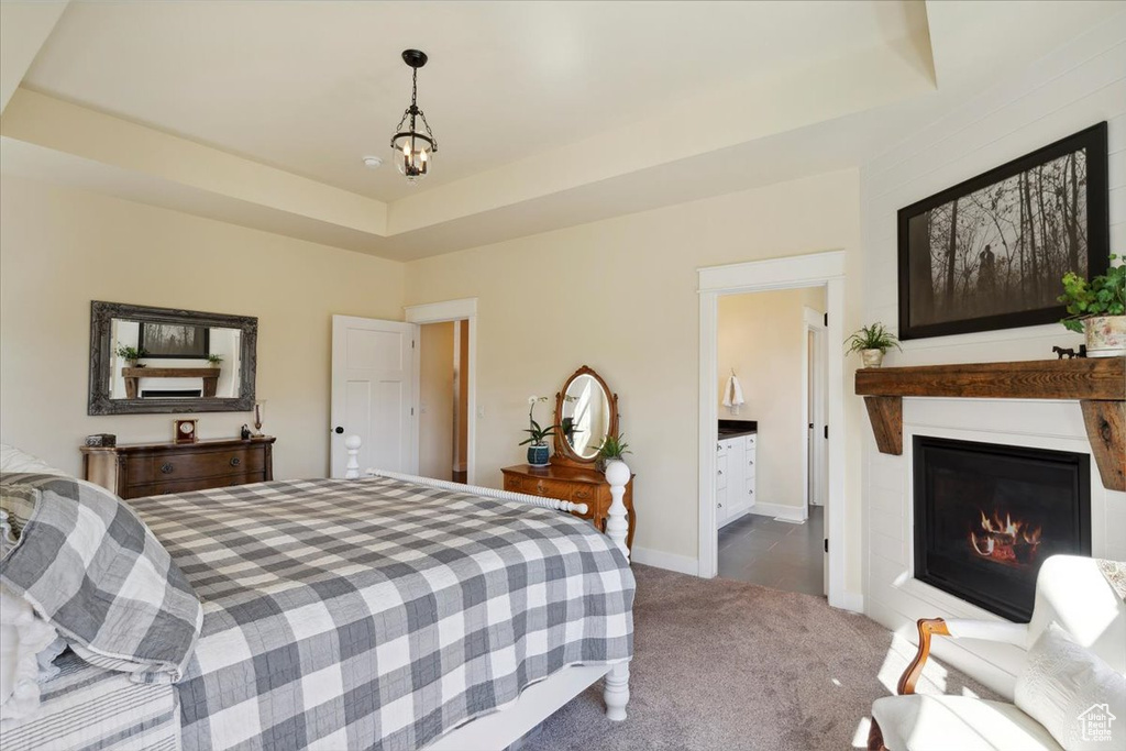 Bedroom featuring a glass covered fireplace, carpet floors, a tray ceiling, baseboards, and a chandelier