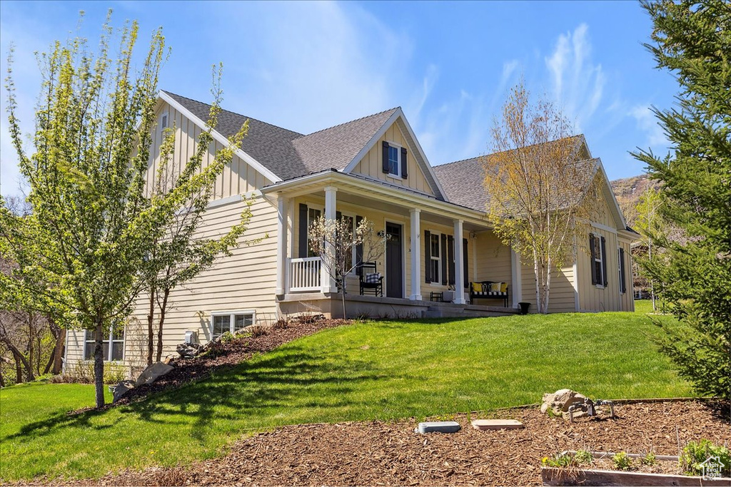 View of front of property with board and batten siding, a front yard, a porch, and a shingled roof