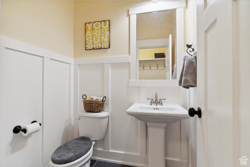 Half bath with toilet, a decorative wall, and a wainscoted wall