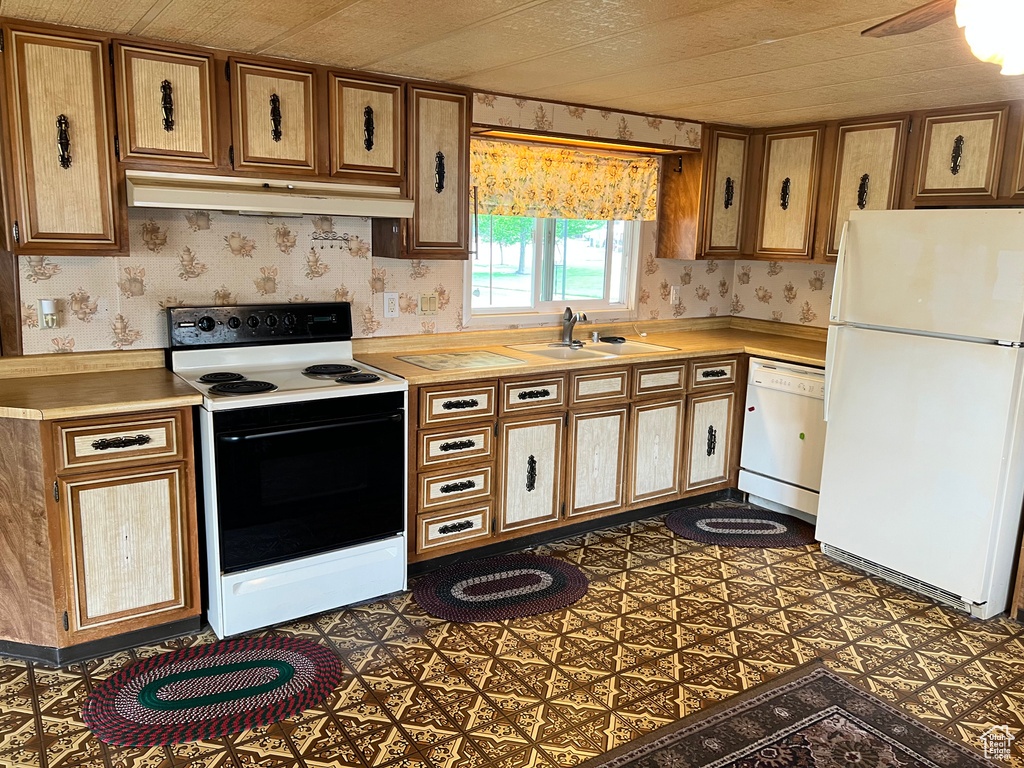 Kitchen featuring white appliances, under cabinet range hood, wallpapered walls, light countertops, and a sink