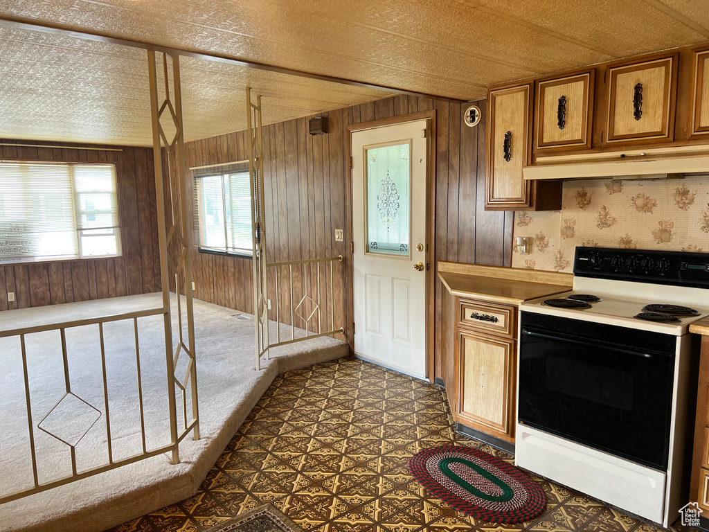 Kitchen featuring electric range, under cabinet range hood, light countertops, brown cabinets, and wood walls