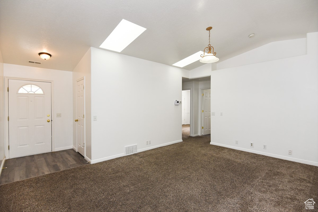 Entrance foyer featuring a skylight, dark colored carpet, vaulted ceiling, and baseboards