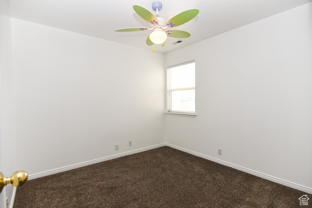 Empty room with dark carpet, baseboards, and a ceiling fan