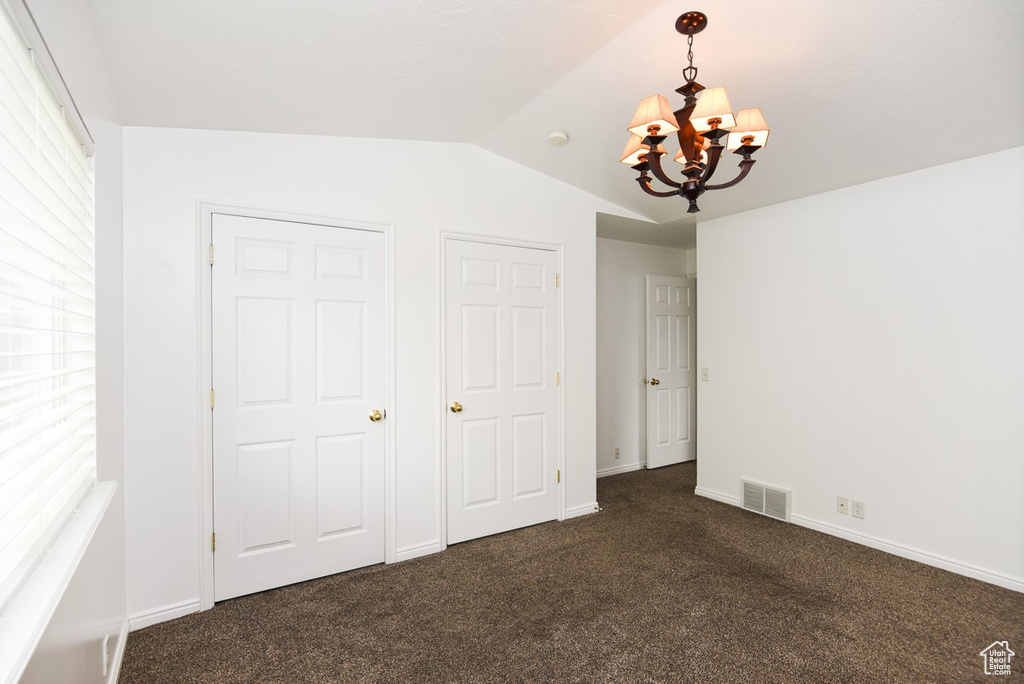 Unfurnished bedroom featuring a chandelier, vaulted ceiling, carpet floors, and baseboards