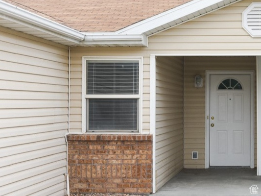 Property entrance featuring brick siding and a shingled roof