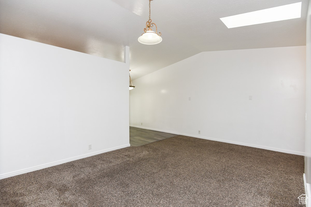 Spare room with a skylight, vaulted ceiling, dark colored carpet, and baseboards