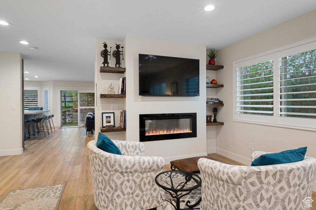 Living room with a glass covered fireplace, light wood-type flooring, baseboards, and recessed lighting