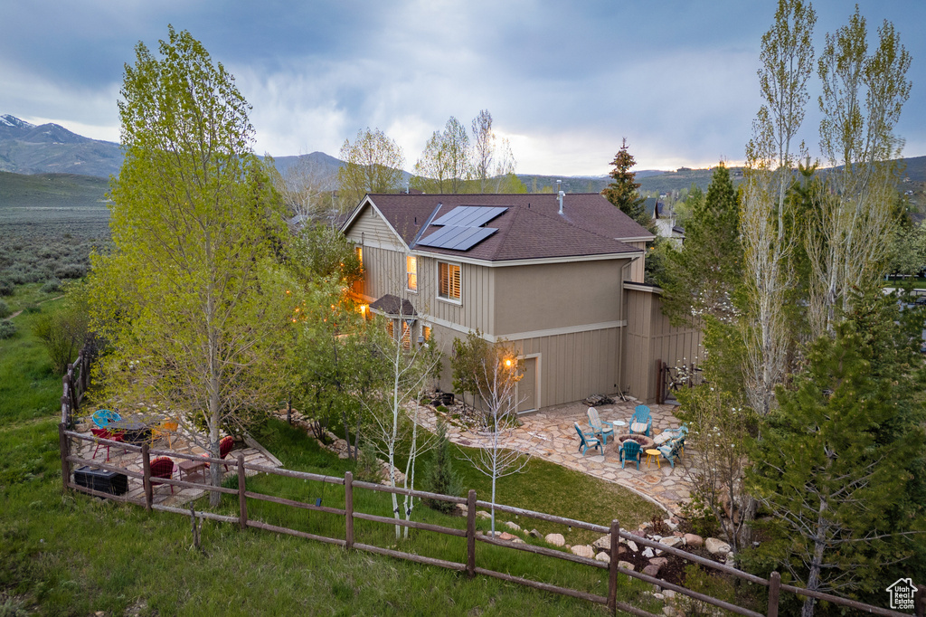 Back of house featuring a patio, solar panels, a mountain view, and roof with shingles