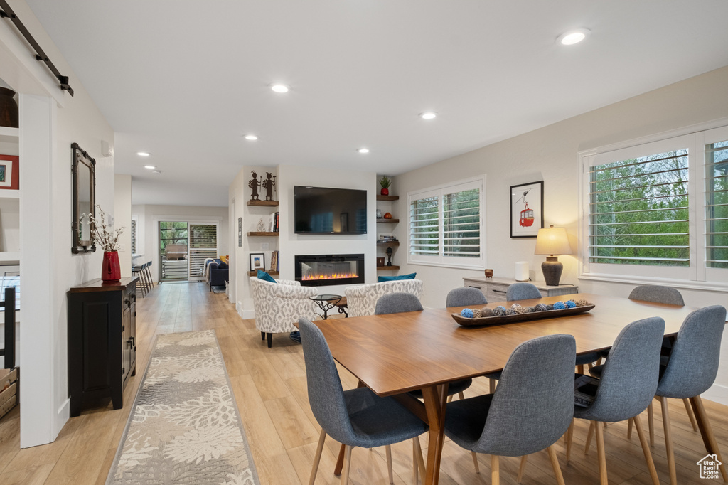 Dining area featuring a barn door, plenty of natural light, a glass covered fireplace, recessed lighting, and light wood finished floors