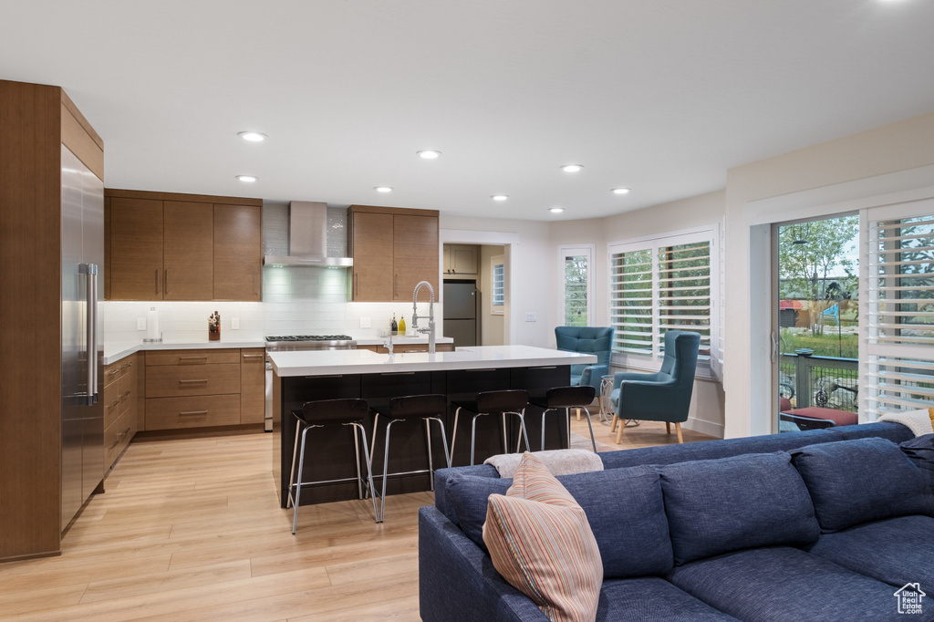Kitchen with wall chimney range hood, open floor plan, a sink, light countertops, and modern cabinets