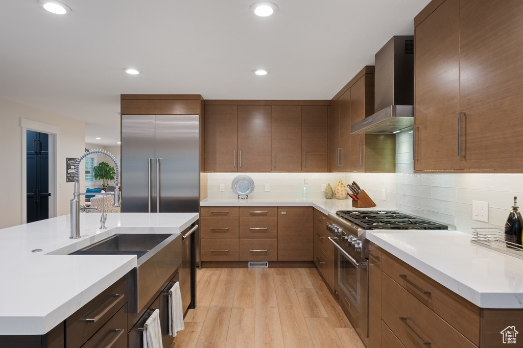 Kitchen featuring high quality appliances, wall chimney range hood, light wood-style floors, light countertops, and recessed lighting