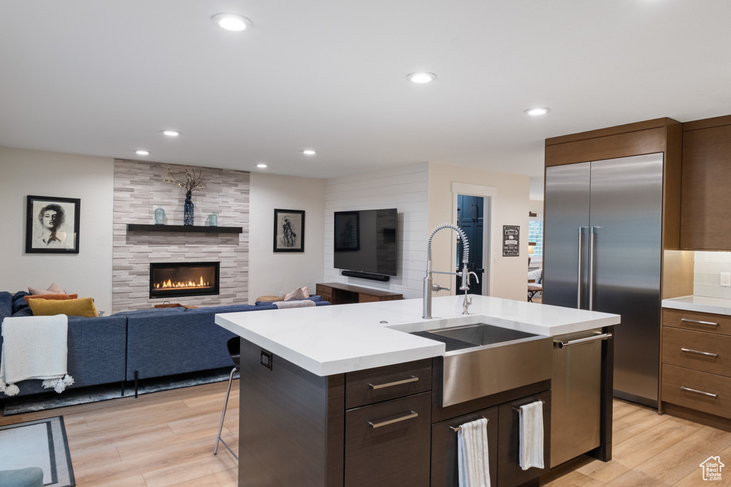 Kitchen with a sink, stainless steel appliances, light countertops, light wood-style floors, and a center island with sink