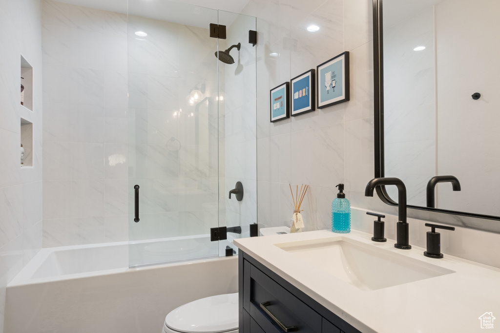 Full bath with toilet, tile walls, vanity, and combined bath / shower with glass door