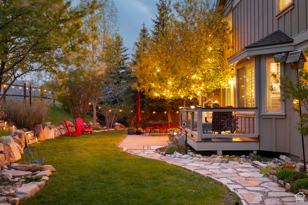 View of green lawn featuring a wooden deck and a patio