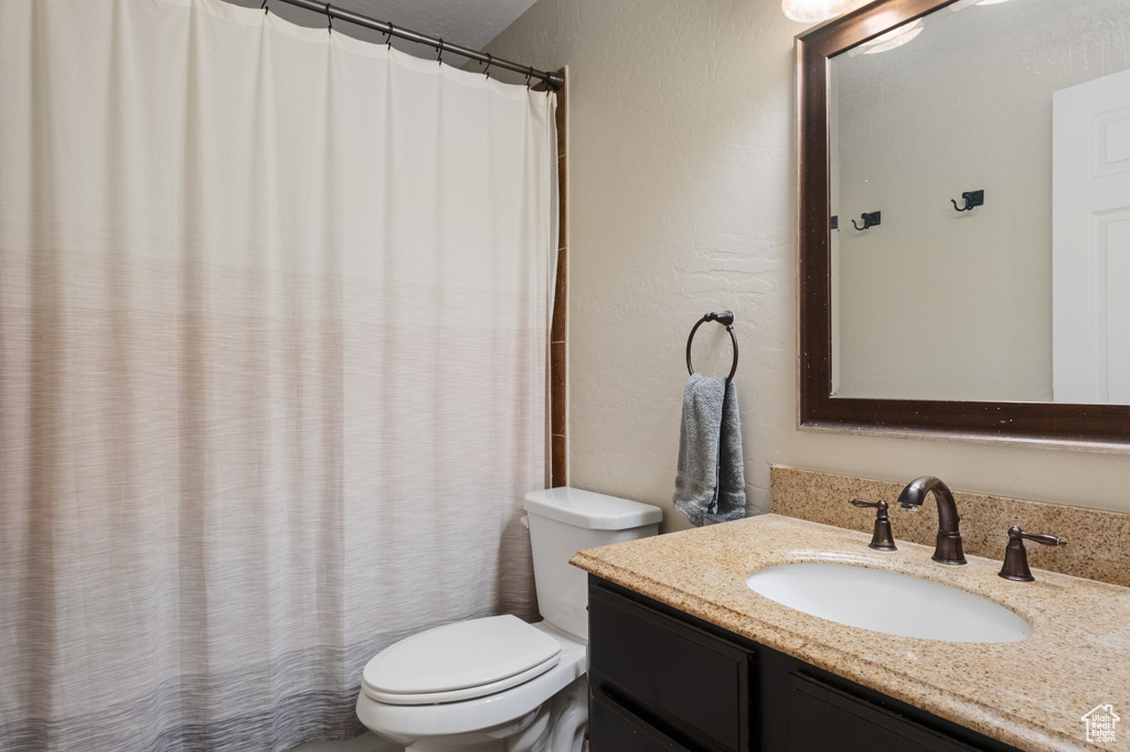 Full bath with toilet, vanity, a textured wall, and a shower with shower curtain