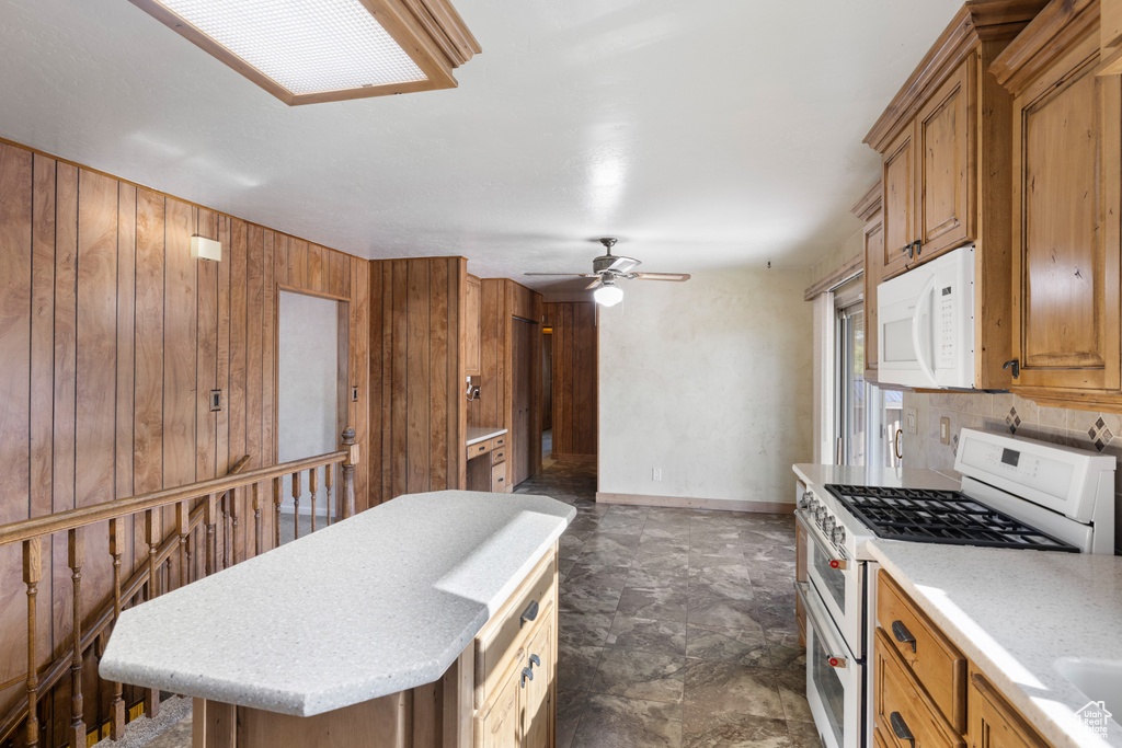 Kitchen featuring white appliances, brown cabinets, wooden walls, a ceiling fan, and light countertops