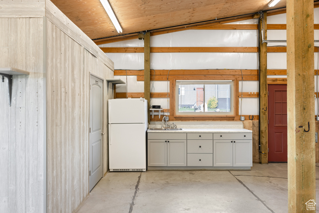 Kitchen with freestanding refrigerator, unfinished concrete flooring, a sink, light countertops, and vaulted ceiling
