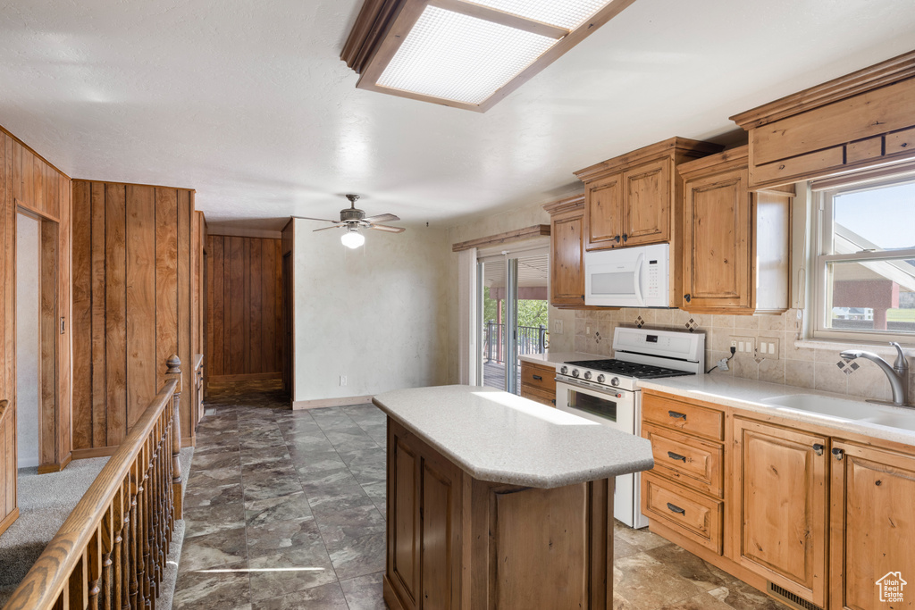 Kitchen with white appliances, a sink, wooden walls, light countertops, and ceiling fan