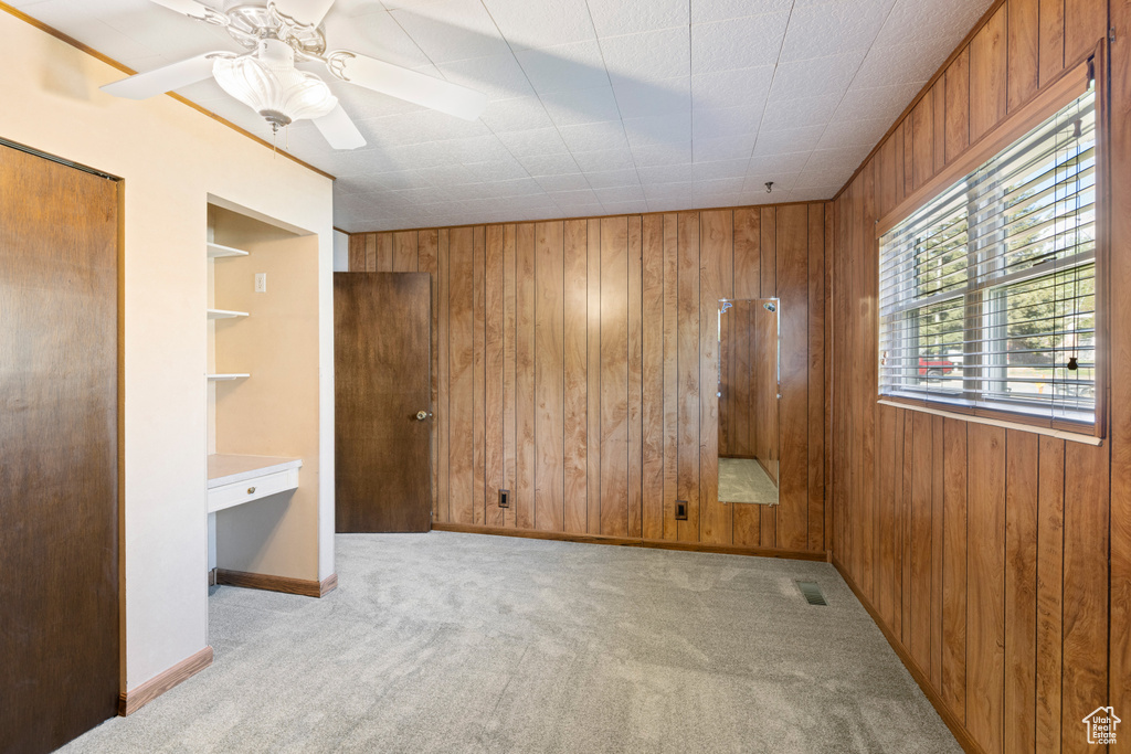 Unfurnished bedroom with wooden walls, carpet flooring, ceiling fan, and baseboards