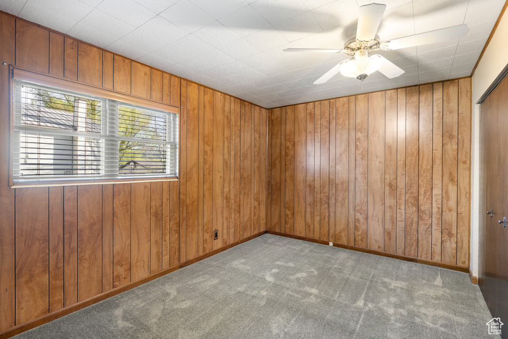Carpeted empty room with wood walls and ceiling fan