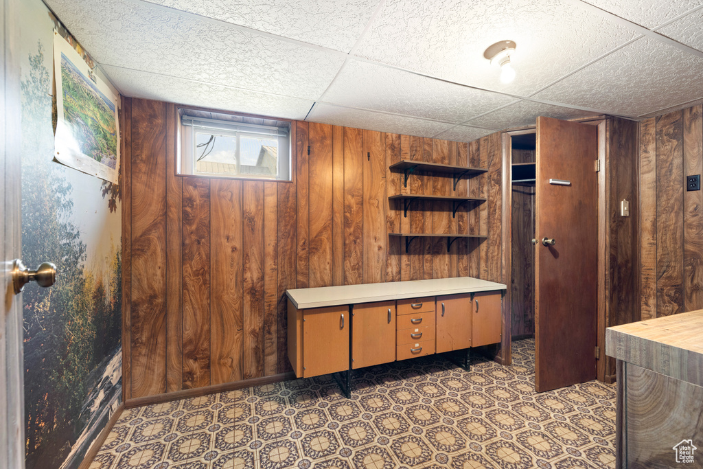 Basement with wooden walls, tile patterned floors, and a paneled ceiling