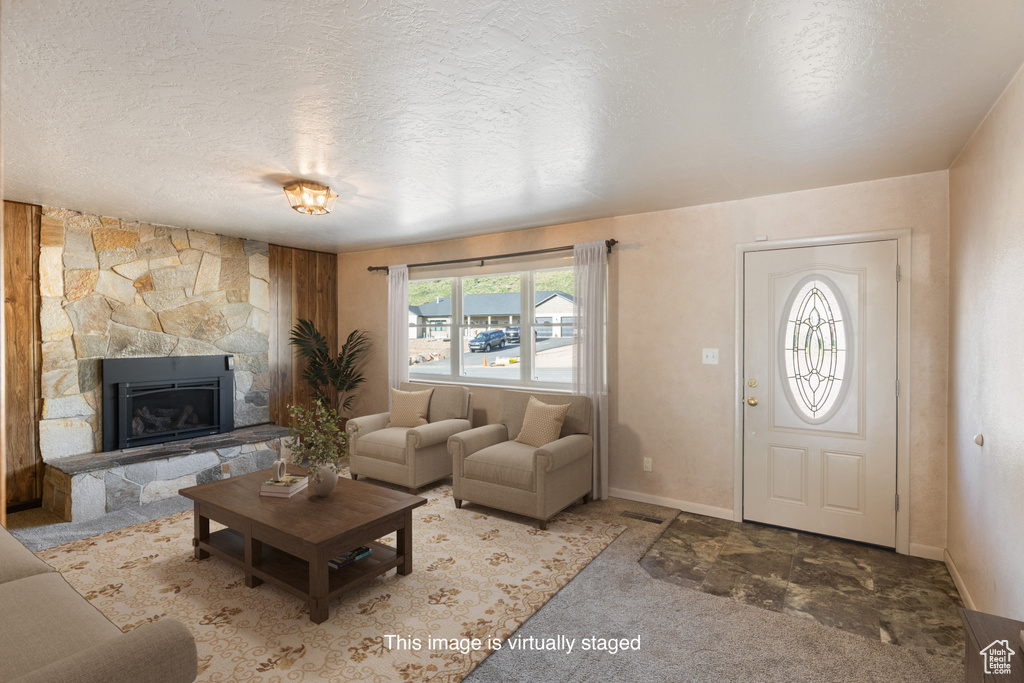 Living room with a textured ceiling, carpet floors, baseboards, and a stone fireplace