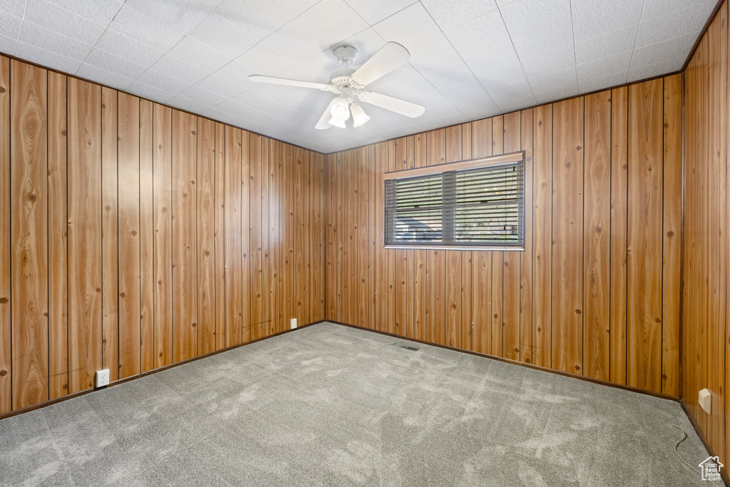 Empty room featuring carpet flooring, ceiling fan, and wooden walls