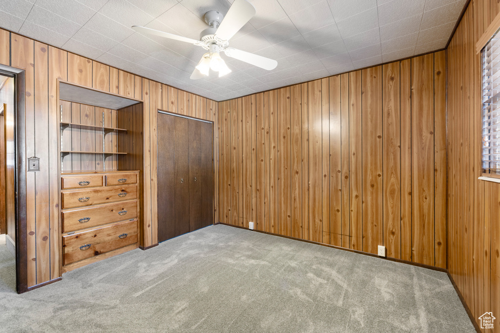Unfurnished bedroom featuring carpet flooring, wooden walls, a closet, and a ceiling fan