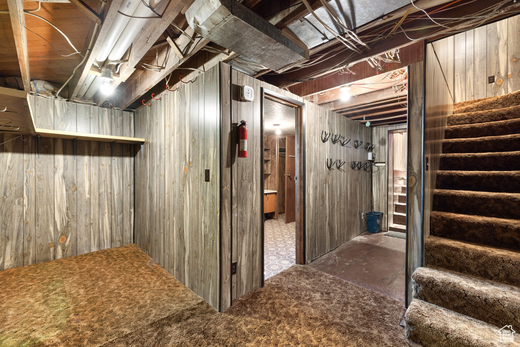 Unfinished basement featuring stairs, wooden walls, and carpet flooring