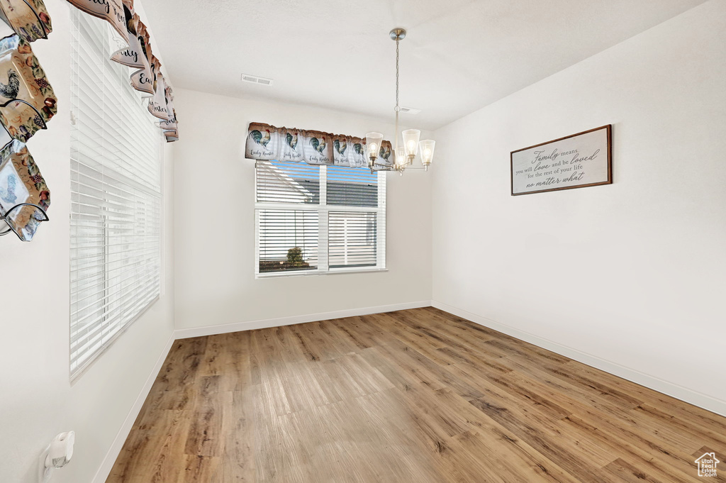 Unfurnished dining area with wood finished floors, a chandelier, and baseboards