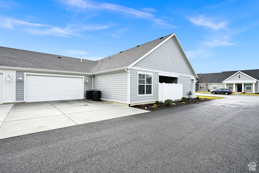 View of property exterior featuring concrete driveway, a garage, a shingled roof, and central air condition unit