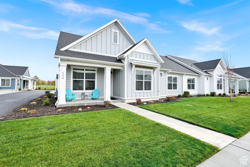 View of front of house featuring board and batten siding, a porch, a front lawn, and a shingled roof
