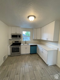 Kitchen featuring appliances with stainless steel finishes, wood finish floors, a sink, white cabinetry, and a textured ceiling