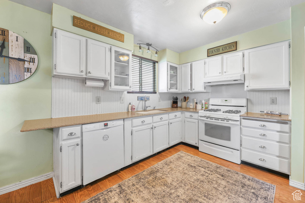 Kitchen with white appliances, under cabinet range hood, white cabinets, and a sink