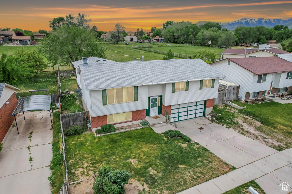 Bi-level home featuring brick siding, driveway, an attached garage, a shingled roof, and a mountain view