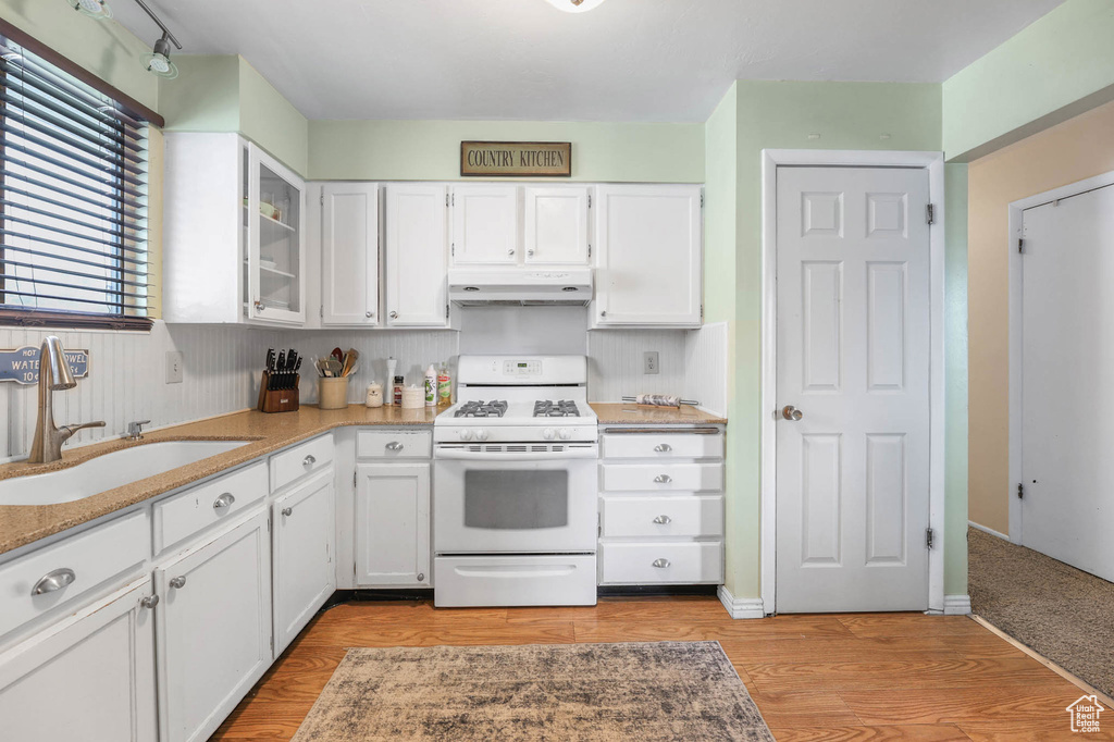 Kitchen featuring white gas range oven, under cabinet range hood, a sink, and white cabinetry
