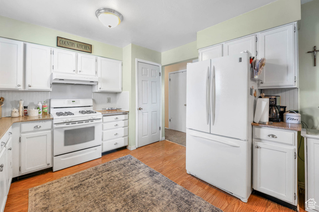 Kitchen featuring white appliances, under cabinet range hood, white cabinets, and light wood finished floors