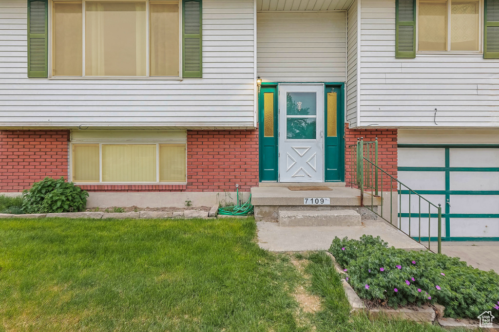 Property entrance featuring brick siding, a garage, and a lawn