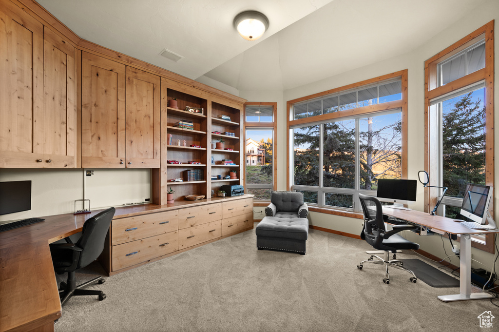 Home office featuring carpet, built in desk, and vaulted ceiling
